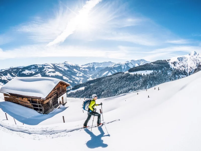 Ein Skitourengeher geht im Tiefschnee bei einer Hütte vorbei