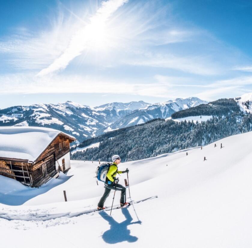 skitouring-kitzbueheler-alpen.jpg Ein Skitourengeher geht im Tiefschnee bei einer Hütte vorbei